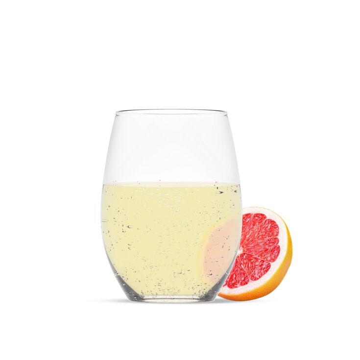 Ein Glas gefüllt mit Sport-Grapefruit-Sirup. Dargestellt mit einem Stück Grapefruit vor weißem Hintergrund.
