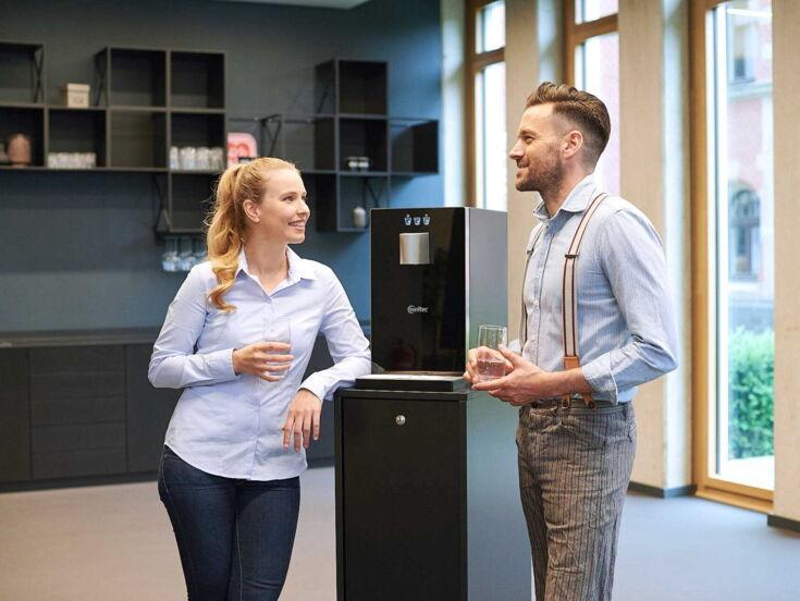 zwei Kollegen stehen am Cube Compact mit Unterschrank und trinken Wasser