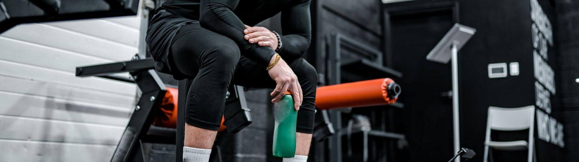 Junger Mann ist im Fitnessstudio und macht Pause mit Sportwasserflasche in der Hand