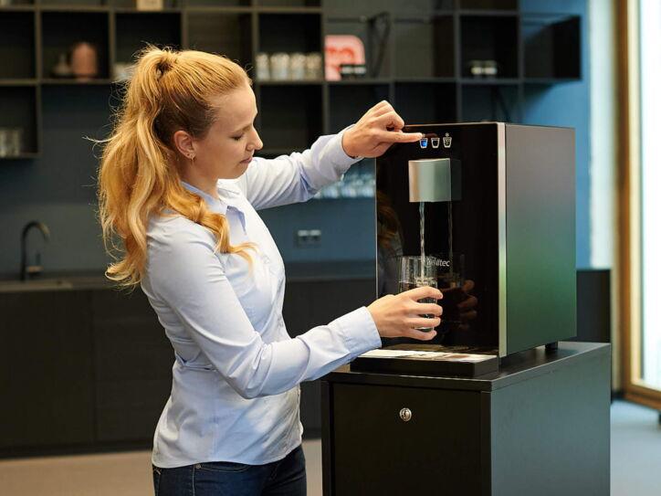 Eine Frau füllt Wasser in ein Glas an einem Wasserspender