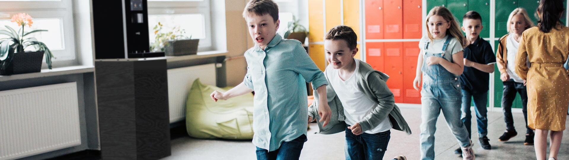 Grundschulkinder laufen über den Flur an Wasserspender vorbei
