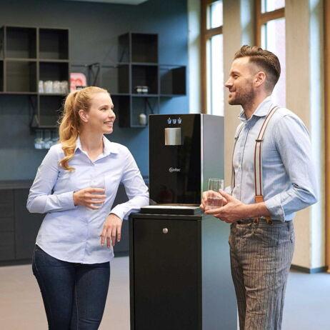 zwei Kollegen stehen am Cube Compact mit Unterschrank und trinken Wasser