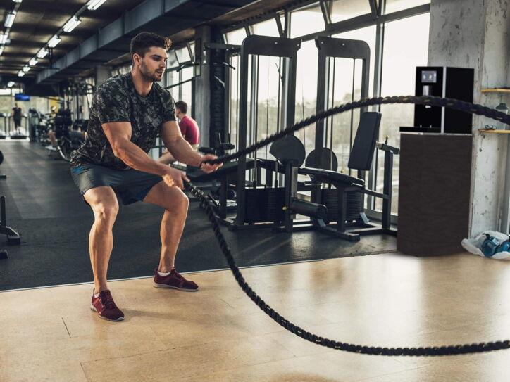 Mann trainiert im Fitnessstudio mit Seilen. Zur Erfrischung befindet sich ein Wasserspender direkt in seiner Nähe.